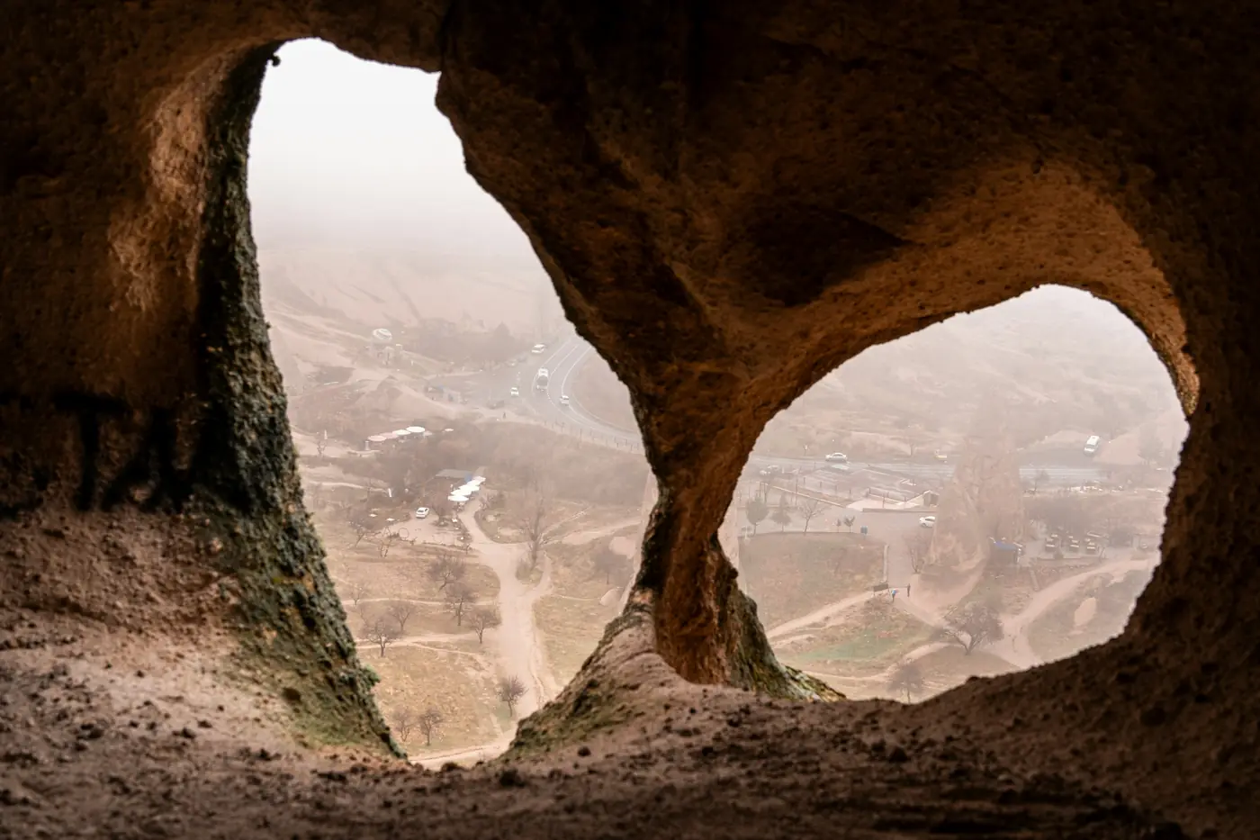 Göreme'de doğal bir kaya kemerinin içinden puslu vadiye ve kıvrılan yola bakış.