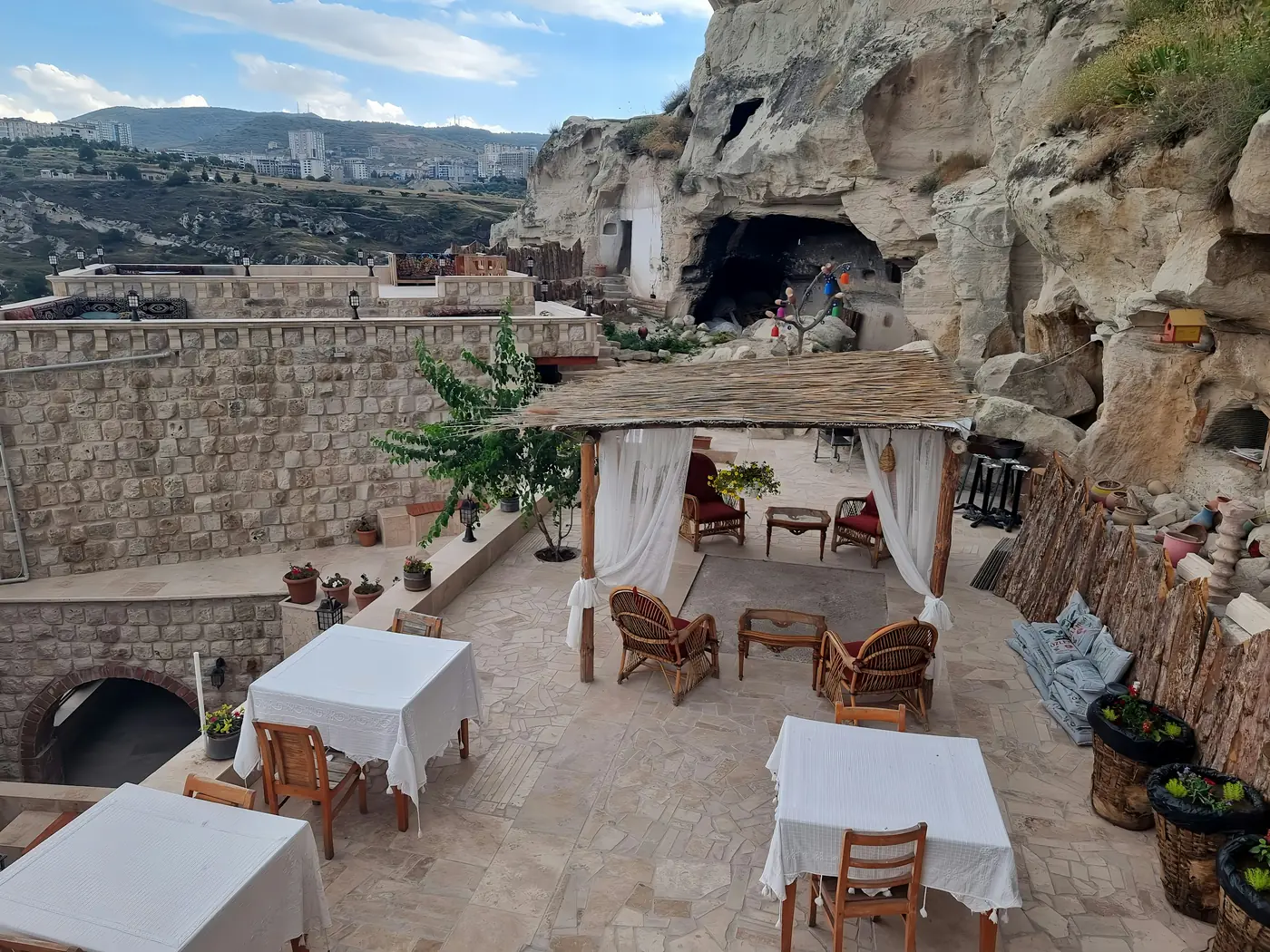 Göreme'de kayaya oyulmuş odaların önünde, beyaz örtülü masaları ve tenteli oturma yeri olan bir taş teras.