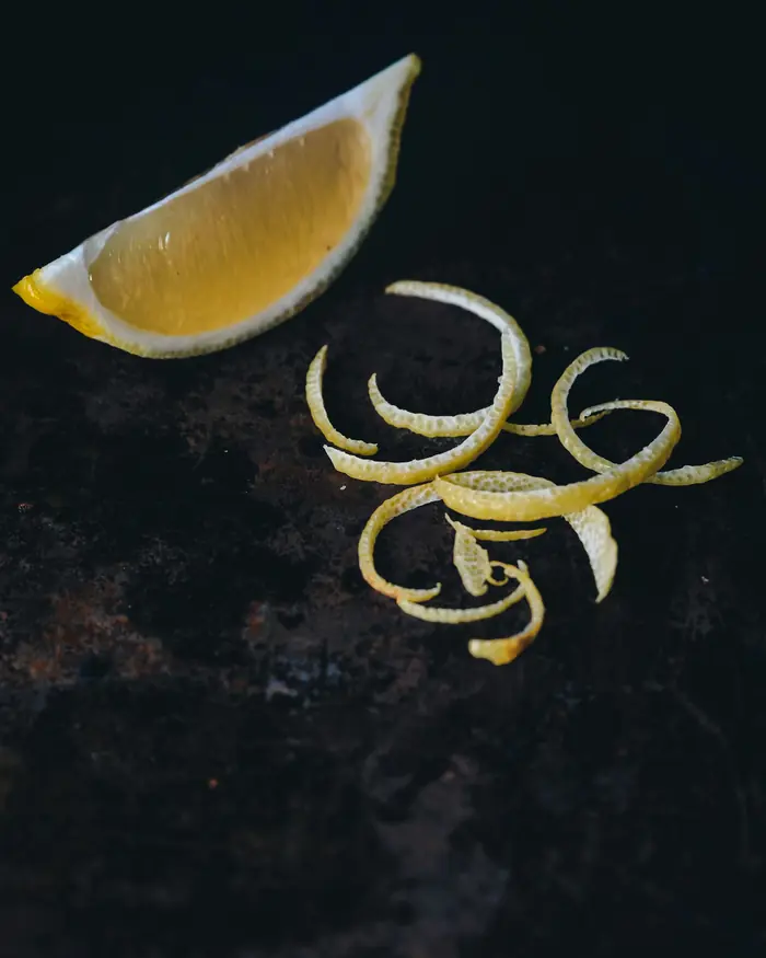 Koyu bir zeminde bir dilim limon ve kıvrılmış limon kabukları