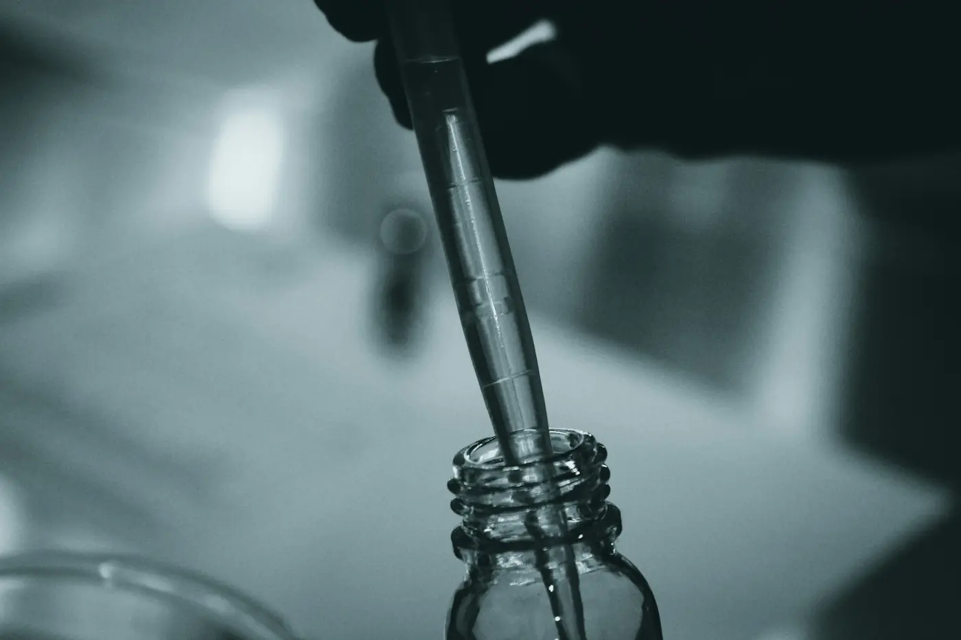 Eldivenli bir el, cam pipetle küçük bir şişeye hammadde alıyor