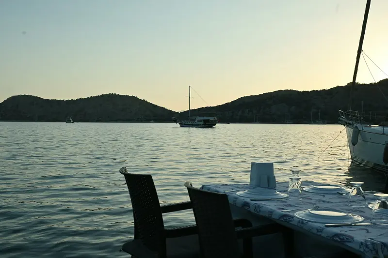 Akşamüstü sakin bir koya bakan güvertede kurulmuş akşam yemeği masası