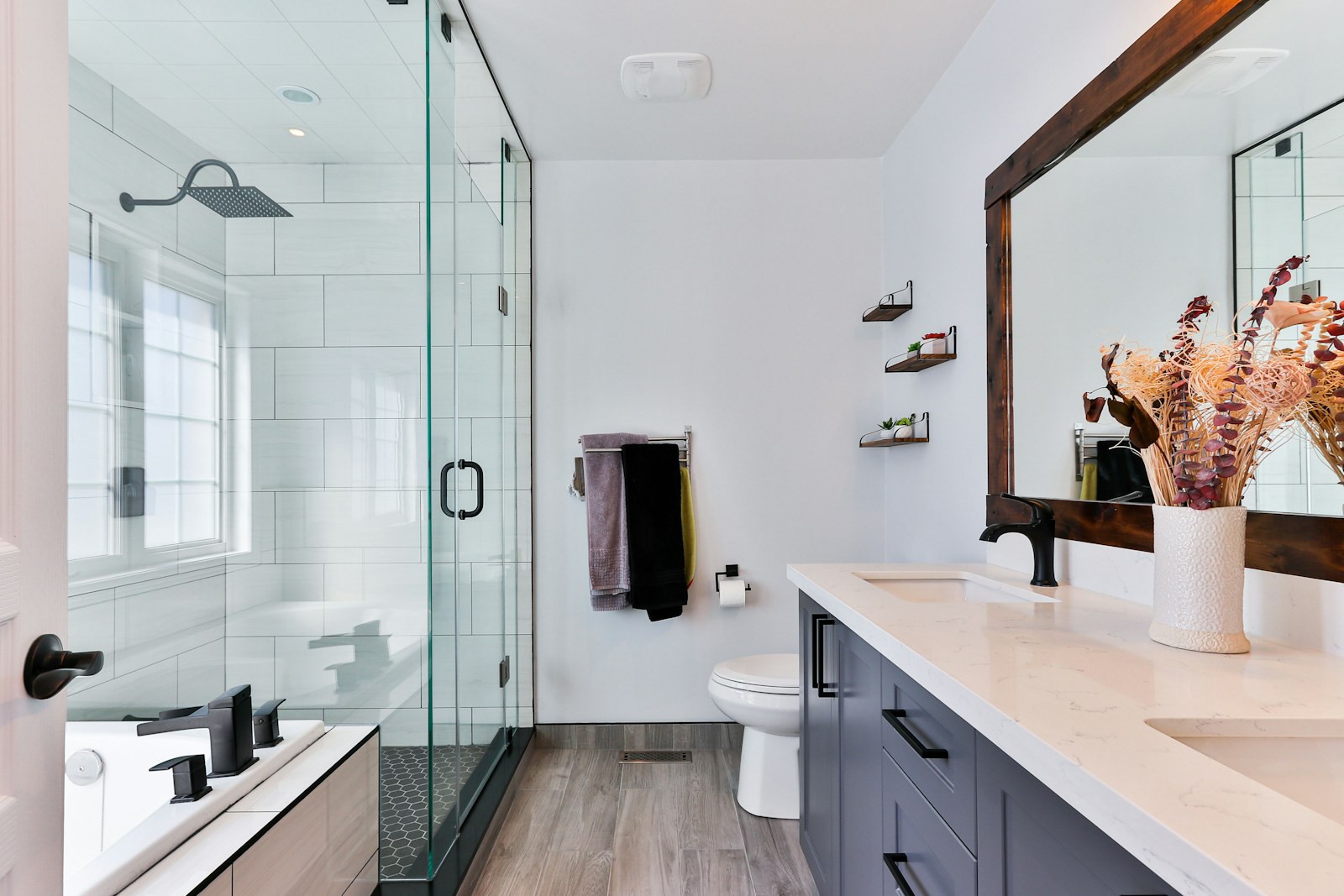 Camlı duşu, geniş tezgâhı ve ahşap çerçeveli aynası olan aydınlık bir banyo