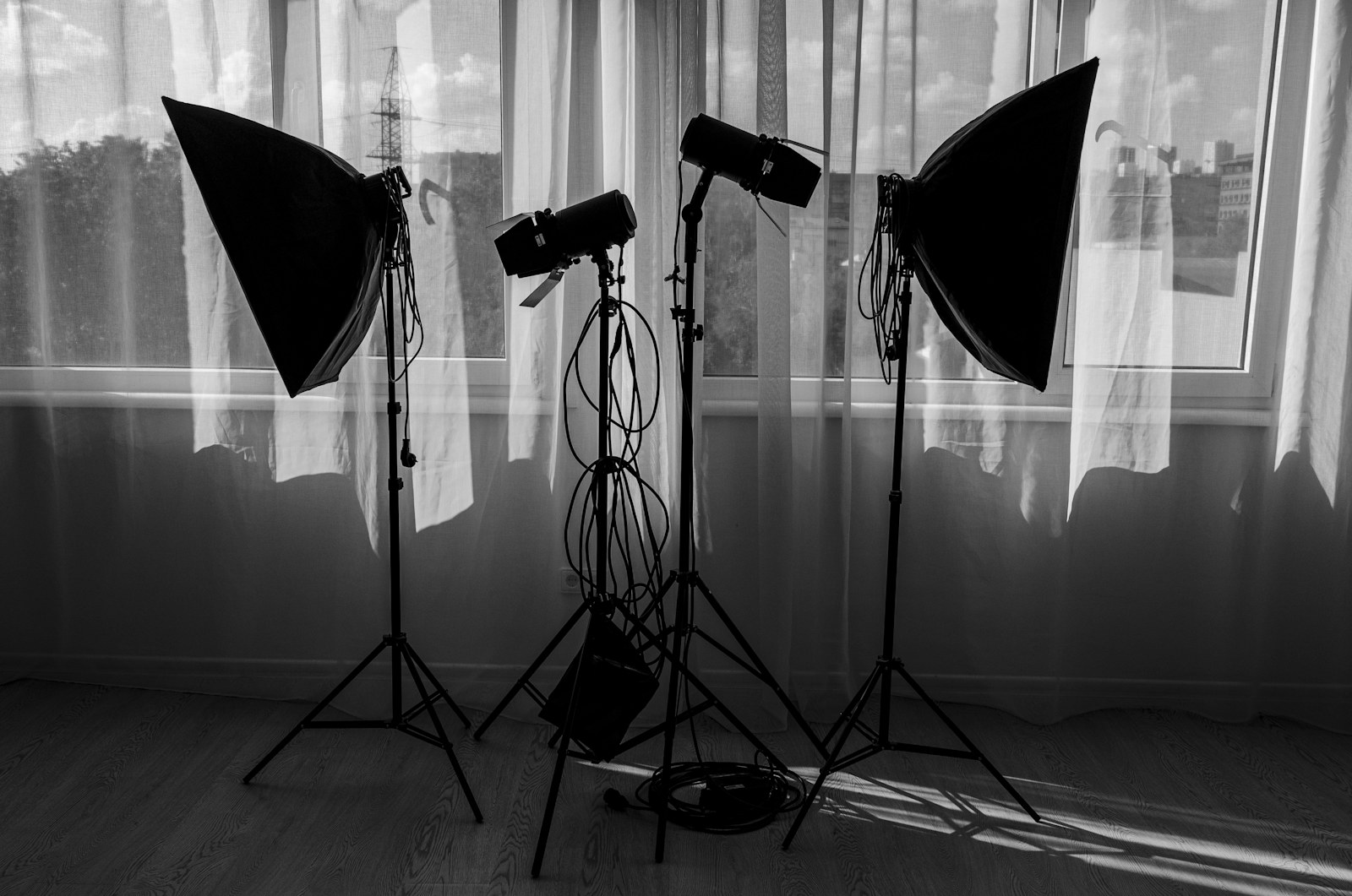 Tül perdeli bir pencerenin önünde, standlar üzerinde duran iki softbox ve iki flaş; siyah beyaz