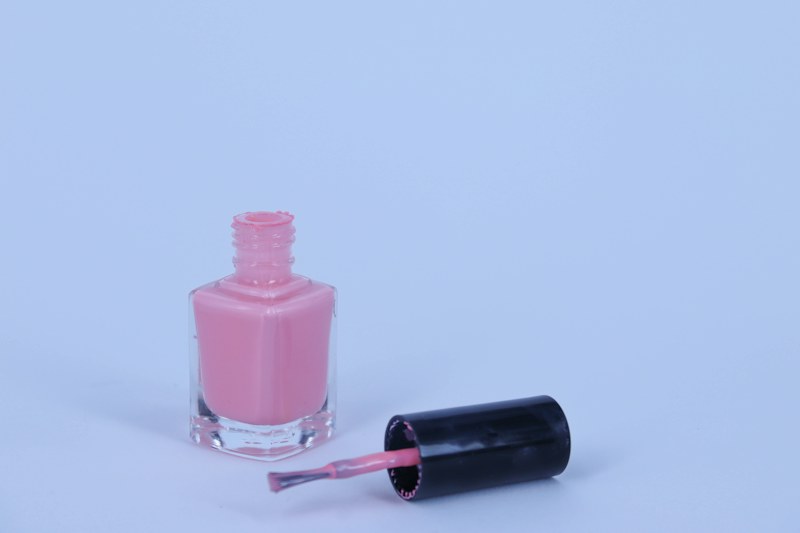 Açık mavi zeminde, kapağı yanında duran açık pembe bir oje şişesi ve fırçası