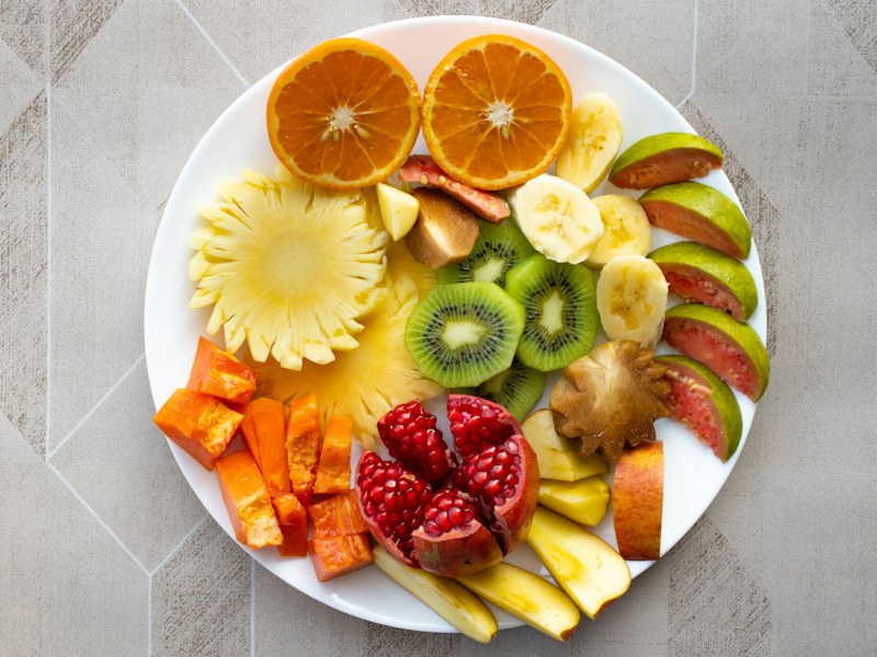 Portakal, ananas, kivi, muz, nar ve havuç dilimleriyle dolu beyaz bir tabak