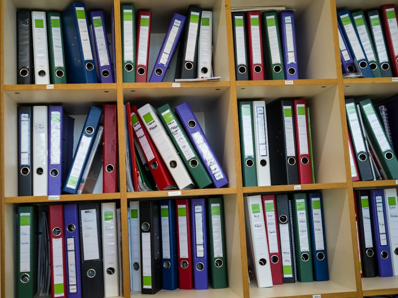 Renkli klasörlerin sıralandığı ahşap bir ofis rafı