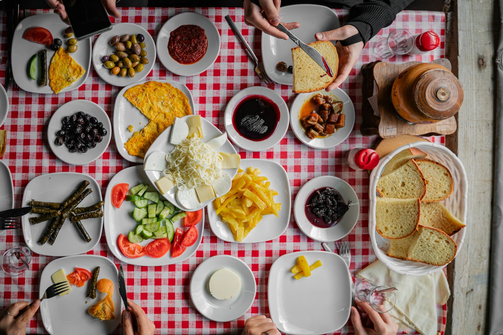 Kırmızı kareli örtüde peynir, zeytin, reçel, sarma ve ekmekle kurulmuş, yukarıdan görülen bir kahvaltı sofrası