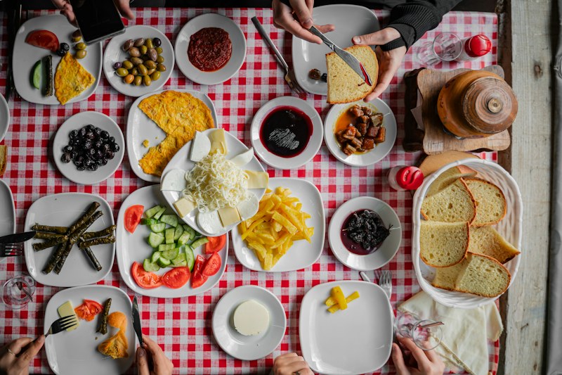 Kırmızı kareli örtüde peynir, zeytin, reçel, sarma ve ekmekle kurulmuş, yukarıdan görülen bir kahvaltı sofrası