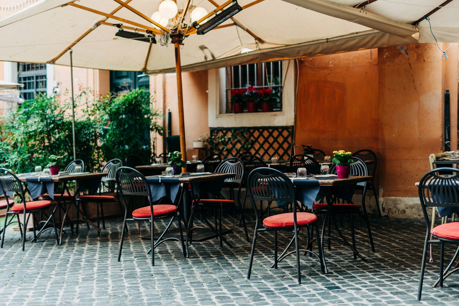Gündüz, şemsiyelerin altında masaları kurulmuş, Arnavut kaldırımlı bir restoran avlusu