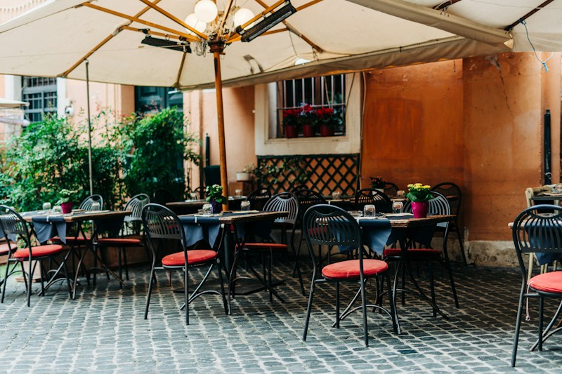 Gündüz, şemsiyelerin altında masaları kurulmuş, Arnavut kaldırımlı bir restoran avlusu