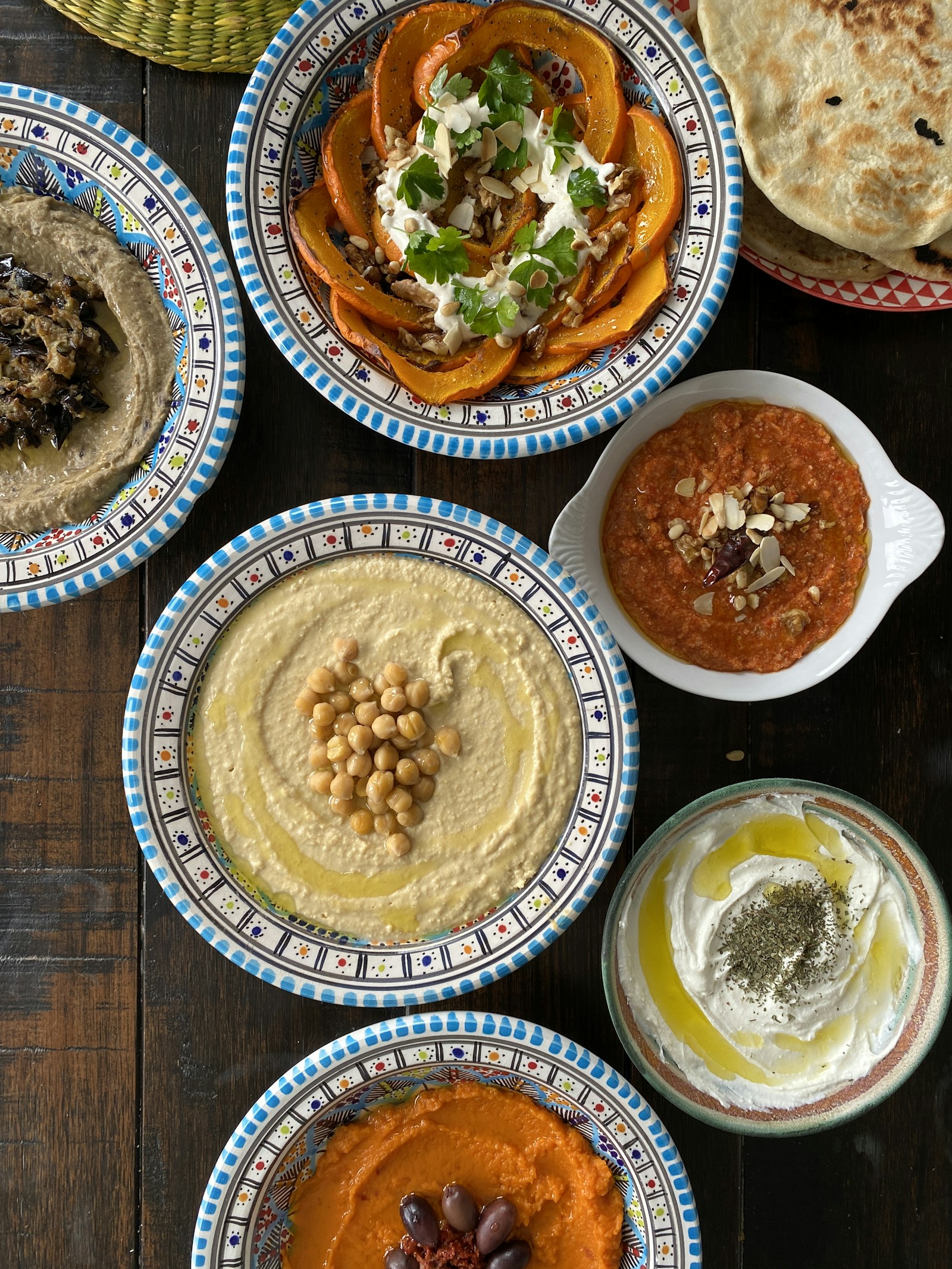 Koyu ahşap masada mavi desenli kâselerde humus, labne, patlıcan ezmesi ve közlenmiş balkabağı