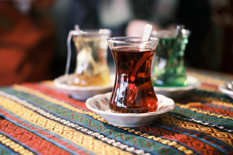 Renkli dokuma bir örtünün üstünde ince belli bardaklarda çay