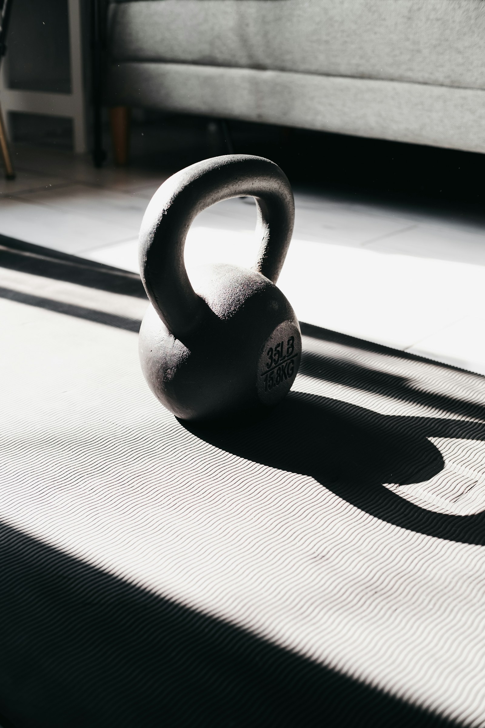 Güçlü güneş ışığında bir matın üstünde duran, uzun gölge düşüren tek bir kettlebell
