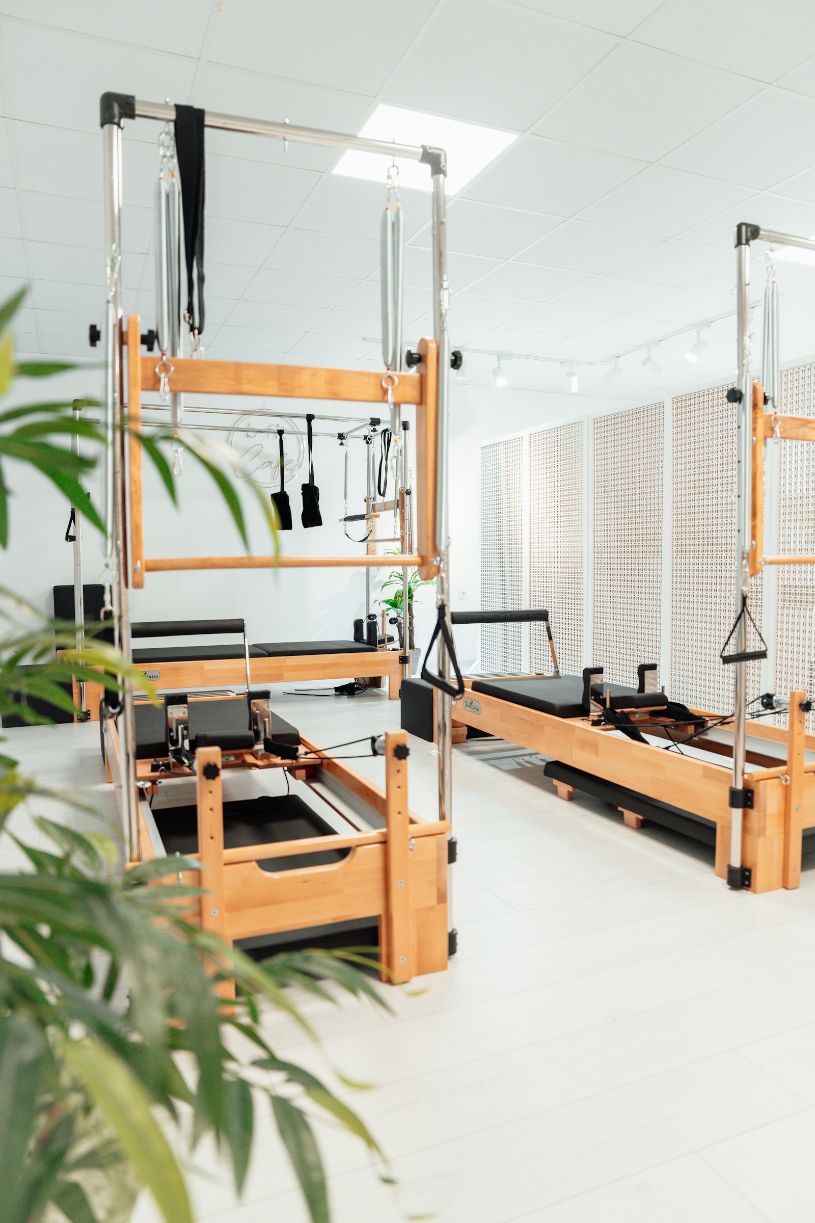 Aydınlık, beyaz bir stüdyoda kule çerçeveli reformer pilates makineleri ve yeşil bitkiler