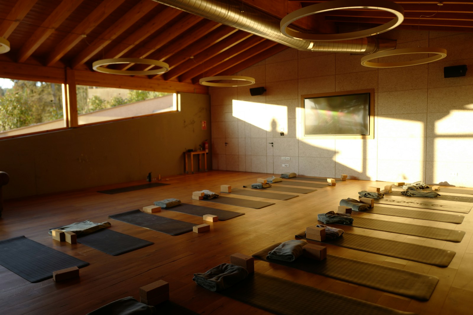 Ahşap zeminde sıralanmış yoga matları, katlanmış havlular ve bloklar; sıcak, güneş vuran bir salon