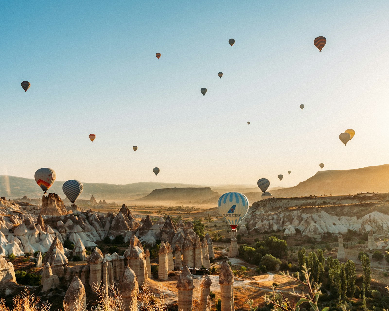 Gün doğarken Kapadokya’da kaya oluşumlarıyla dolu bir vadinin üstünde süzülen sıcak hava balonları