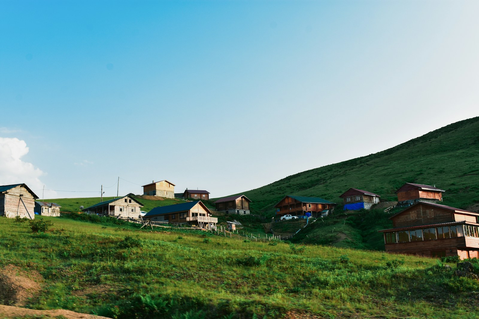 Yeşil bir yaylada, mavi gökyüzünün altında yamaca dizilmiş ahşap evler